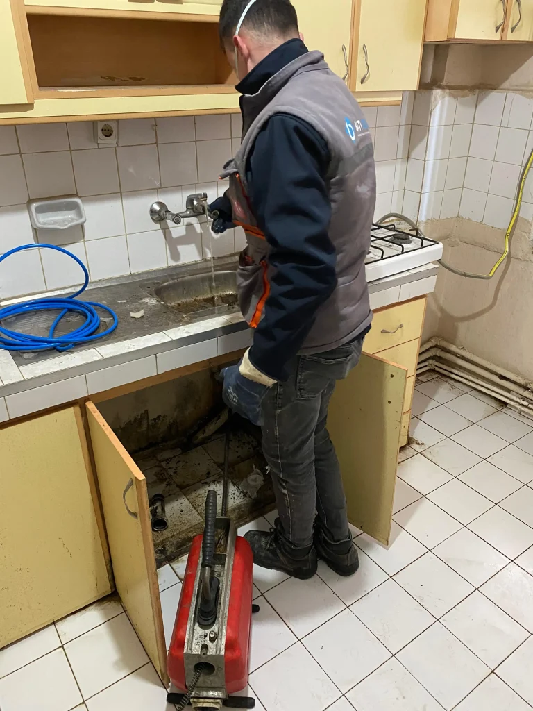 Muratlı tıkalı lavabo açma çalışmasında mutfak tezgahının altındaki gider borusuna elektro-mekanik robot cihazla müdahale eden usta.