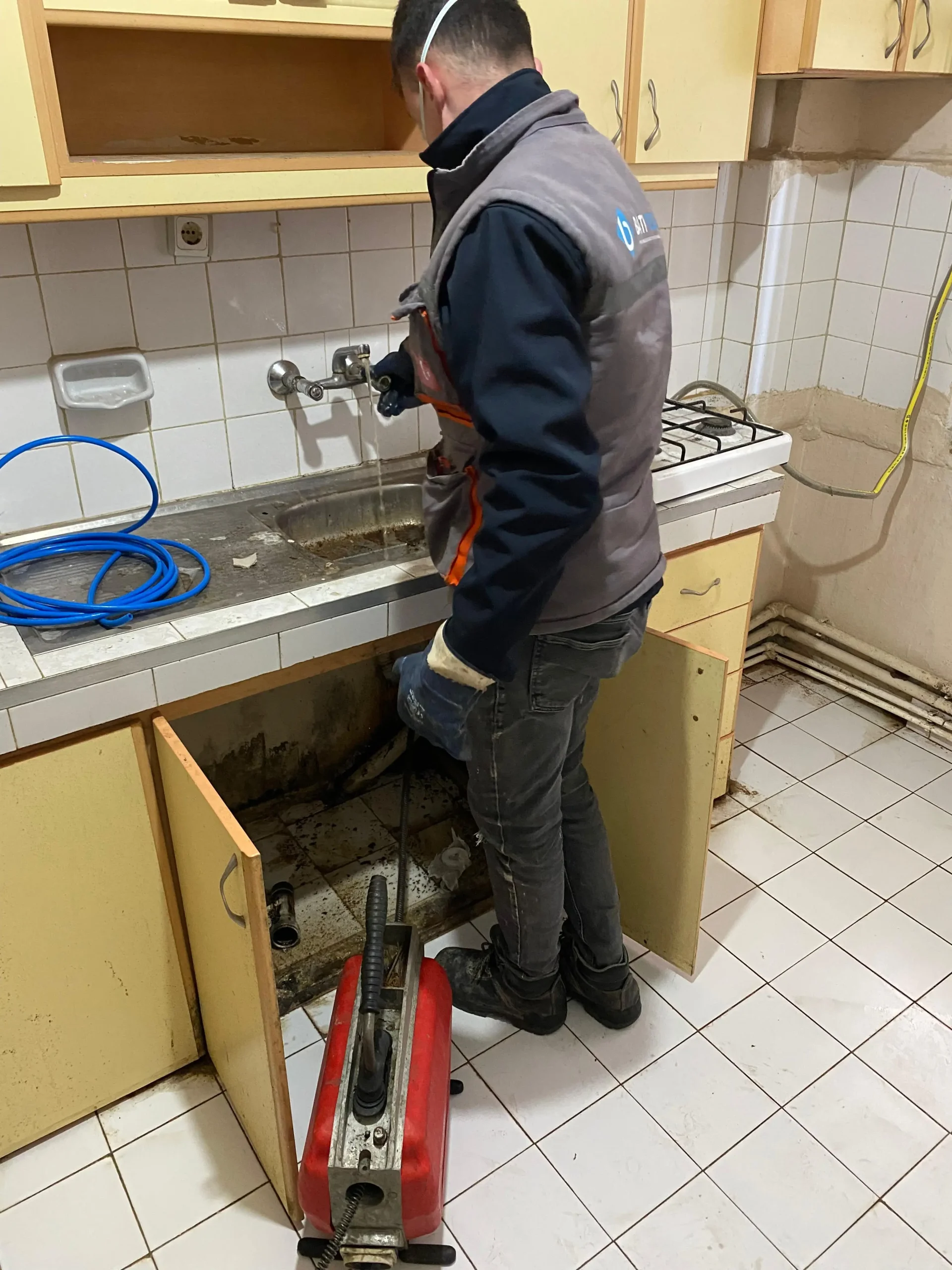 Muratlı tıkalı lavabo açma çalışmasında mutfak tezgahının altındaki gider borusuna elektro-mekanik robot cihazla müdahale eden usta.